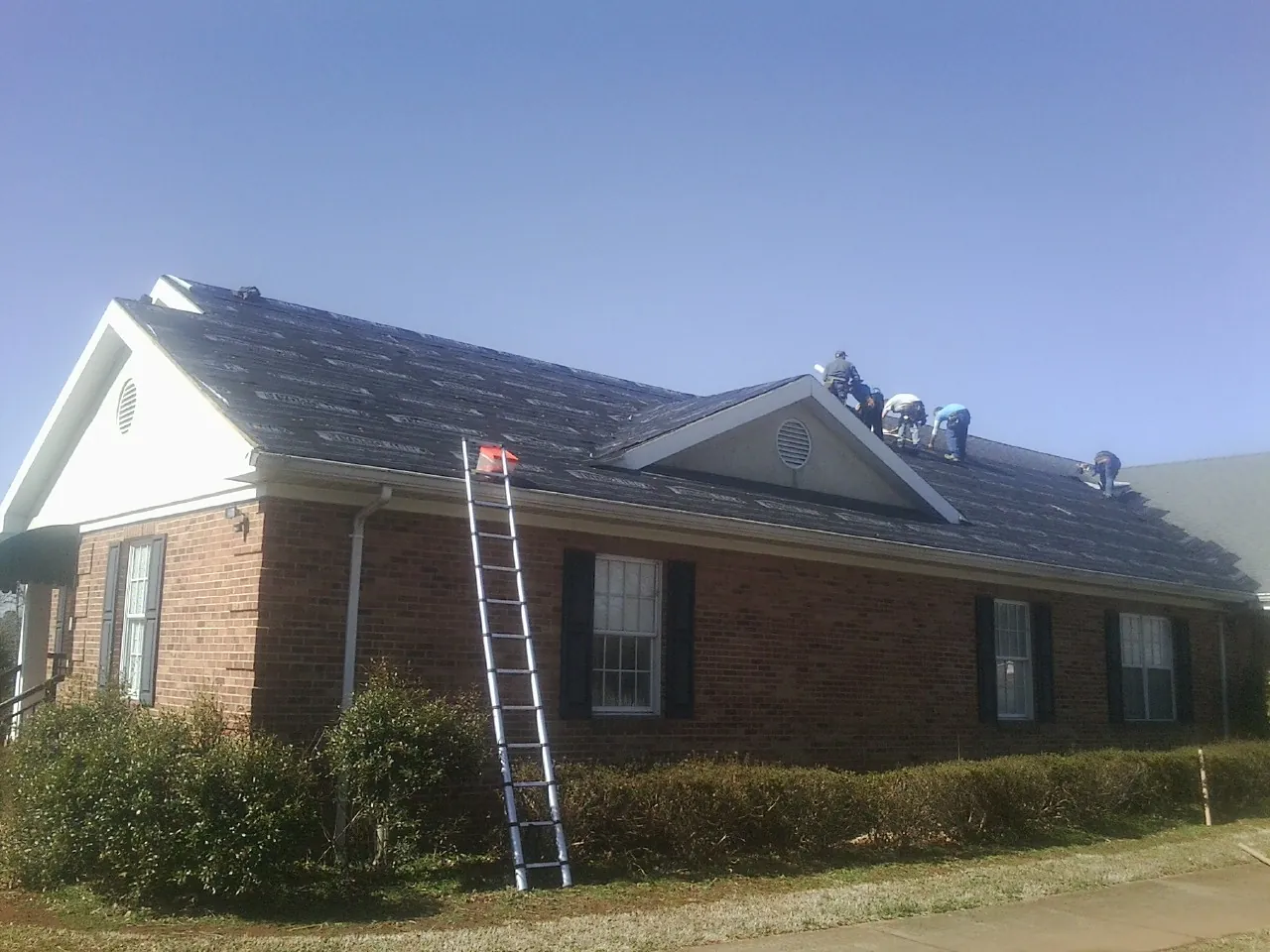 Crew tearing shingles off a brick ranch roof with a ladder set — Metal Roof Repair work by our crew in Corydon