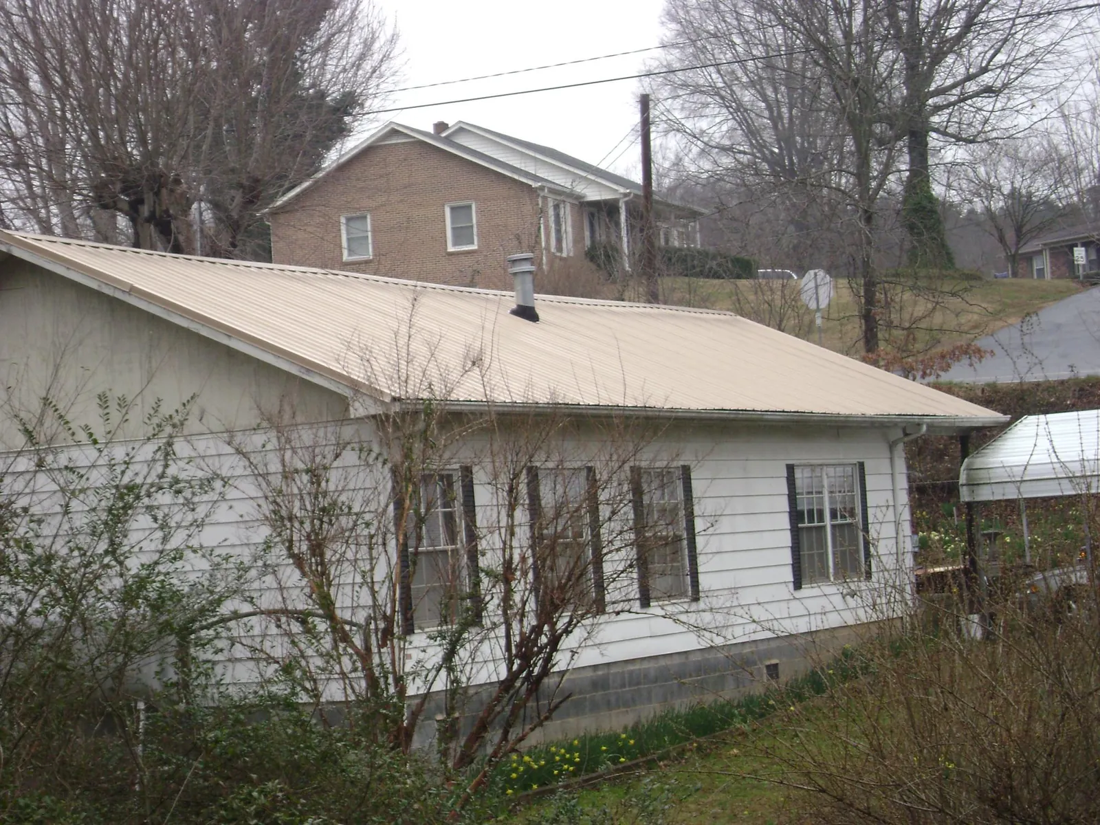 Tan metal roof on a white sided house set into a hillside — Commercial Roofing by Roofing Brothers in Corydon
